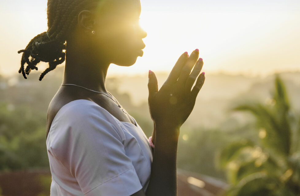 Woman praying with sunset behind her